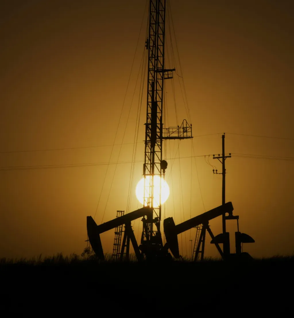 Oil pumpjacks and a drilling rig at sunset